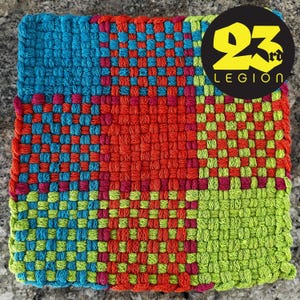 Puede incluir: Textil cuadrado tejido en colores vibrantes. El diseño se divide en cuatro cuadrantes: azul, rojo, verde y una mezcla de rosa y azul. El texto "23rd LEGION" está en un círculo negro en la esquina superior derecha.