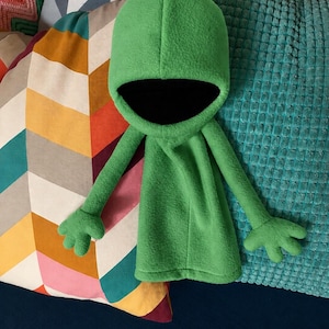 May include: A bright green fleece hooded garment featuring a deep, rounded hood with a black interior lining, long sleeves, and four-fingered hand-shaped ends. The piece has a smooth, soft texture and a simple, loose-fitting silhouette.