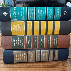 May include: A stack of vintage Reader's Digest Condensed Books in various colors. The books have gold lettering and titles such as "Best Sellers," "The Death Committee," and "Once Upon an Island."