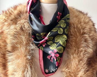 May include: A black silk scarf with a pink border and a floral print. The scarf is tied around a wooden mannequin and is partially covered by a brown fur collar.