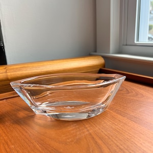 May include: A clear glass bowl with a slightly curved shape. The bowl is sitting on a wooden surface.