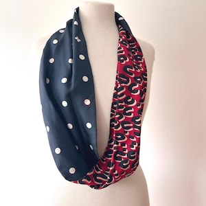 May include: A reversible infinity scarf with a navy blue polka dot pattern on one side and a red and black animal print on the other. The scarf is displayed on a mannequin.