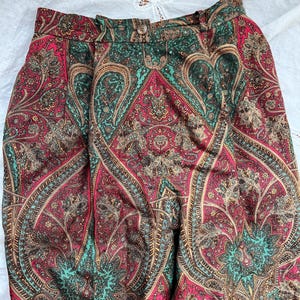 May include: High-waisted pants with a vibrant paisley pattern in shades of red, teal, and brown. The fabric features intricate, detailed designs. The pants have a button and zipper closure.