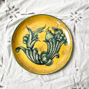 May include: A yellow ceramic plate with a green and white design of stylized fruit and leaves.