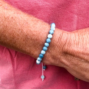 以下が含まれることがあります： 白の紐で結ぶ留め具が付いた、青と白のビーズブレスレットです。