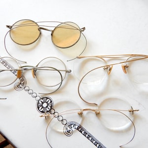 May include: An assortment of vintage eyeglasses with wire frames. The glasses feature round and oval lenses in various styles, including tinted and clear options. The frames are primarily silver and gold-toned, showcasing a classic, antique aesthetic.
