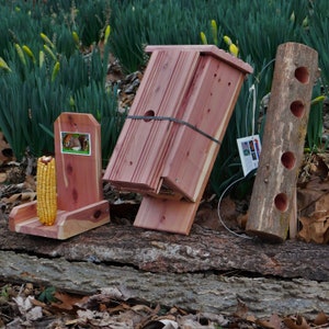 Puede incluir: Tres comederos de ardilla de madera hechos de cedro. El comedero de la izquierda es un soporte para mazorcas de maíz. El comedero del medio es una casita de pájaros con un panel frontal extraíble. El comedero de la derecha es un tronco con tres agujeros perforados.