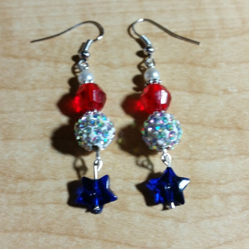 May include: A pair of red, white, and blue star-shaped dangle earrings. The earrings feature a red, white, and blue bead design with a star-shaped charm at the bottom.