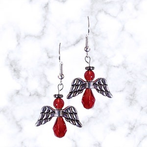 Pu&ograve; includere: Un paio di orecchini pendenti a forma di angelo in argento con accenti di cristallo rosso.