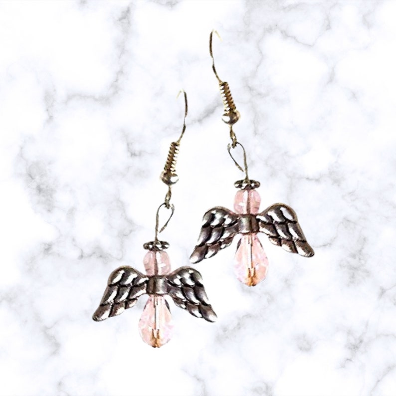 Pu&ograve; includere: Un paio di orecchini pendenti a forma di angelo in argento con accenti di cristallo rosa.
