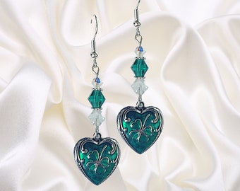 May include: Dangle earrings with heart-shaped pendants in green enamel, featuring a silver clover design. The earrings have silver hooks and are decorated with clear and green crystal beads. The earrings are approximately 6 cm in length.
