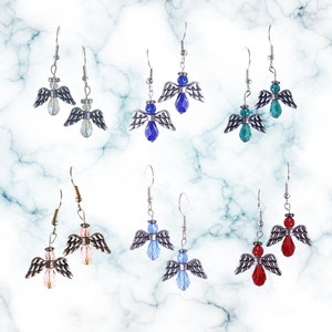 Pu&ograve; includere: Sei paia di orecchini pendenti con ciondoli a forma di angelo in argento e dettagli in cristallo. I cristalli sono di vari colori, tra cui blu, rosa, rosso e verde.