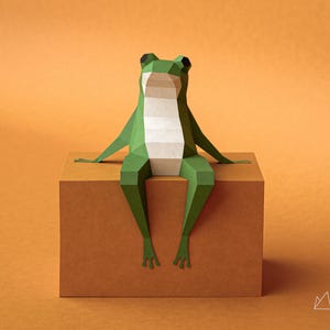 Pode incluir: Uma rã de papel geométrica em tons de verde e branco sentada numa caixa castanha sobre um fundo laranja. O corpo da rã é feito de papel dobrado, com as pernas penduradas na borda. O logotipo Paper Valley está no canto inferior direito.