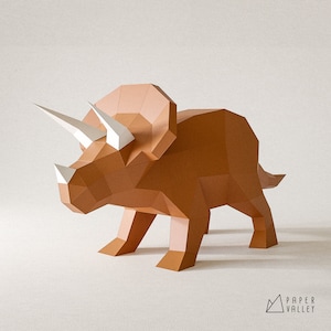 May include: A brown papercraft model of a Triceratops dinosaur. The model has three horns on its head and a frill around its neck. The model is standing on a white surface.