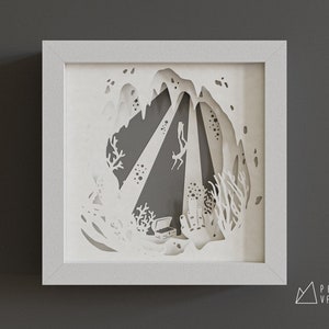 May include: White paper cut-out art depicting a diver exploring a cave with a treasure chest at the bottom. The art is framed in a white frame.