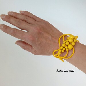 May include: A bright yellow beaded bracelet with a cluster of larger beads in the center. The bracelet is worn on a person's wrist.