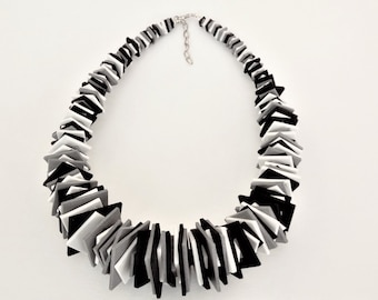 Puede incluir: Un collar geométrico negro, blanco y gris hecho de cuadrados apilados. El collar está hecho por Katarina Silk.