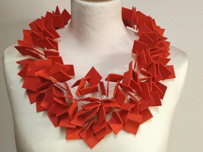 May include: A red necklace made of many small, geometric shapes. The necklace is made of paper or cardboard and is strung together with wire.