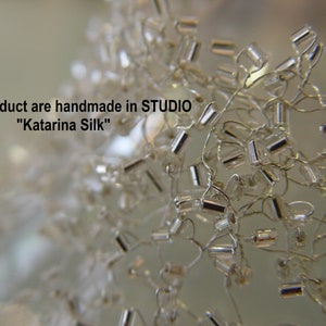 May include: Close-up of a silver beaded necklace with small, rectangular beads. The beads are strung on thin wire and are arranged in a random pattern. The necklace is handmade in the "Katarina Silk" studio.