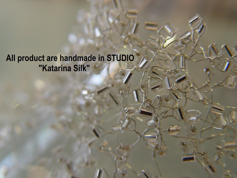 May include: Close-up of a silver beaded necklace with small, rectangular beads. The beads are strung on thin wire and are arranged in a random pattern. The necklace is handmade in the "Katarina Silk" studio.