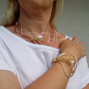 May include: A gold and silver wire necklace and bracelet set with a pearl accent. The necklace is a delicate, multi-layered design, while the bracelet is a single, curved band.