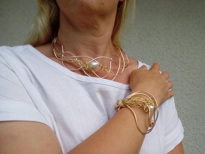 May include: A gold and silver wire necklace and bracelet set with a pearl accent. The necklace is a delicate, multi-layered design, while the bracelet is a single, curved band.