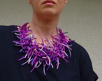 May include: A purple, white, and lavender necklace made of thin, twisted cords. The necklace is layered and has a messy, organic look.