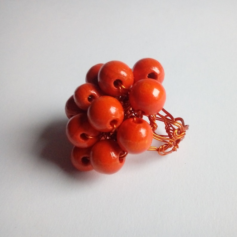 May include: A cluster of orange wooden beads are woven together with copper wire to create a unique ring.
