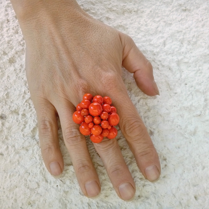 May include: A large, bright orange ring made of many small, round beads. The ring is worn on a person's finger.