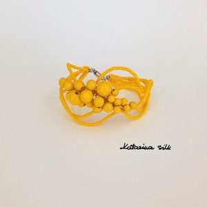 May include: A yellow beaded bracelet with a cluster of round beads in the center. The bracelet is made of multiple strands of small beads and has a silver clasp.