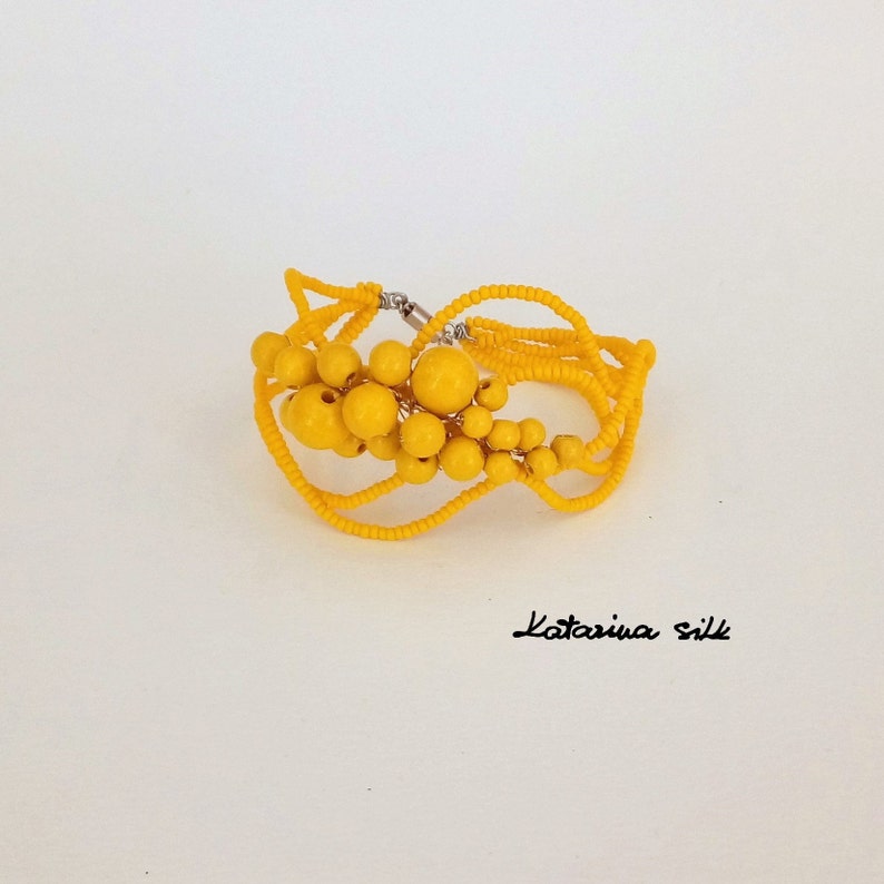 May include: A yellow beaded bracelet with a cluster of round beads in the center. The bracelet is made of multiple strands of small beads and has a silver clasp.