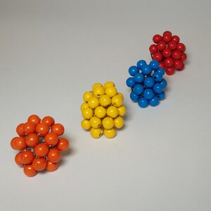May include: Four colorful beaded rings, each made of small, round beads clustered together in a sphere shape. The rings are red, blue, yellow, and orange.