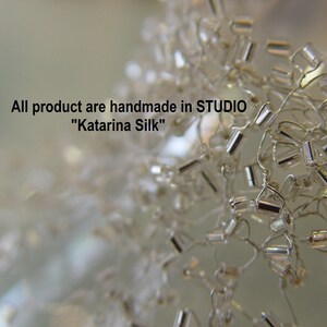 May include: Close-up of a silver beaded necklace. The beads are small and cylindrical, and they are strung together in a delicate pattern. The necklace is handmade in the "Katarina Silk" studio.
