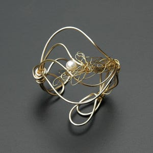May include: A gold wire bracelet with a single pearl accent. The wire is twisted and formed into a delicate, organic shape.