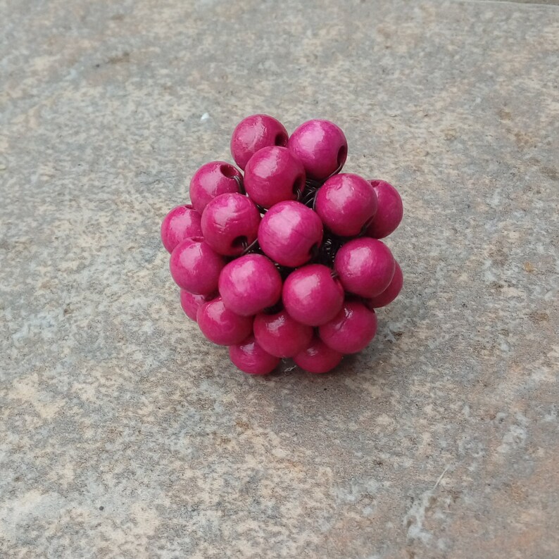 May include: A cluster of pink wooden beads strung together with wire. The beads are arranged in a sphere shape.