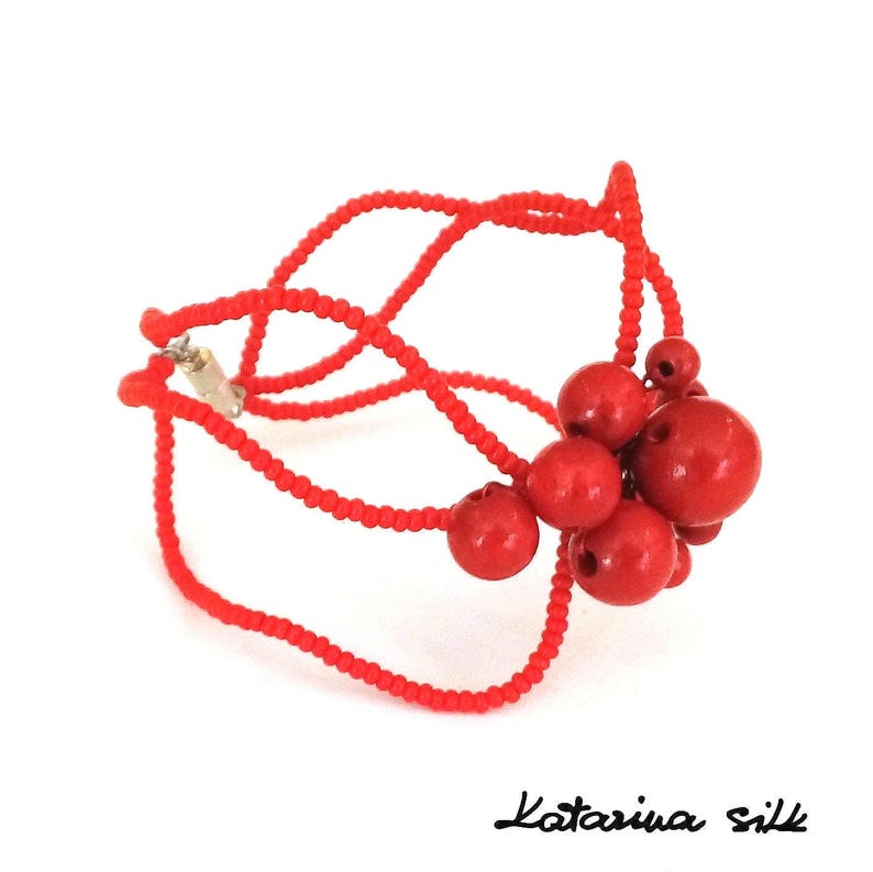 May include: A red beaded bracelet with a cluster of red beads in the center. The bracelet is made of small, red beads that are strung together in a delicate pattern. The cluster of beads is made of larger, round beads that are also red. The bracelet is a beautiful and unique piece of jewelry.