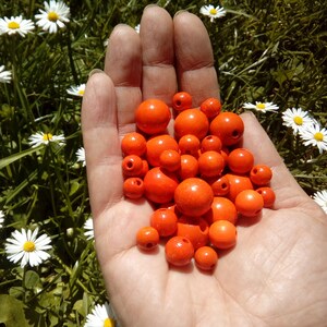 May include: A hand holding a pile of bright orange wooden beads. The beads are round and smooth, and they are all about the same size.