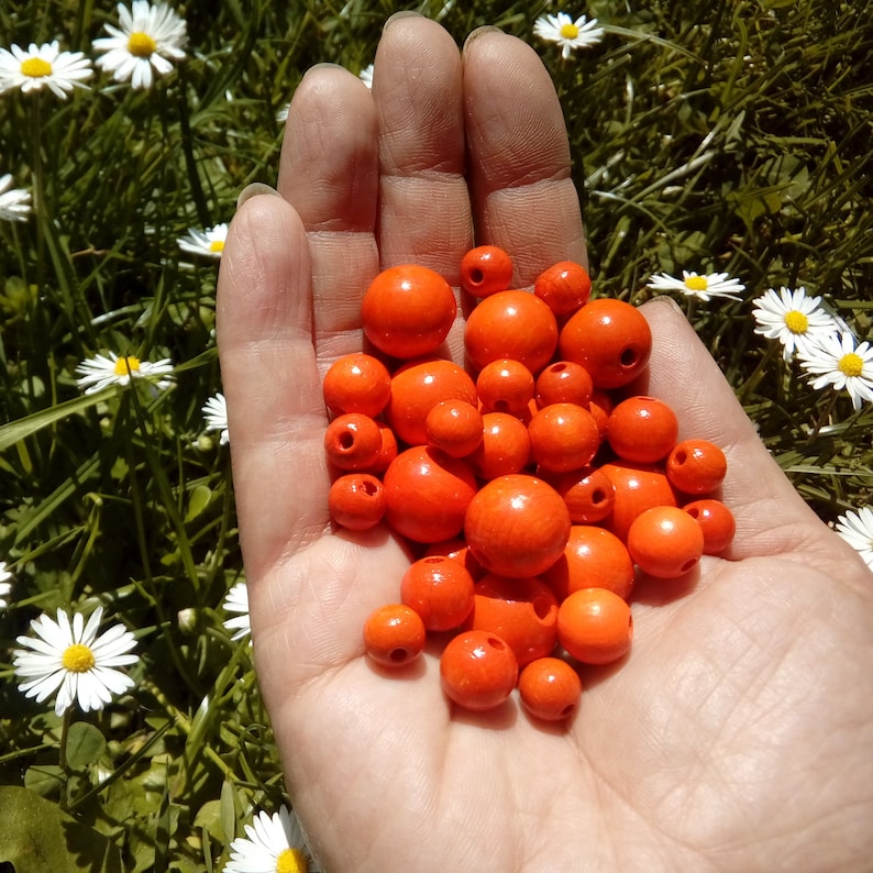 May include: A hand holding a pile of bright orange wooden beads. The beads are round and smooth, and they are all about the same size.