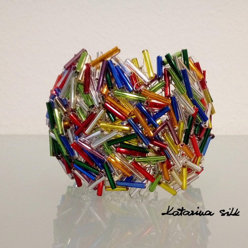 May include: A colorful sphere made of glass rods in various colors, including red, green, blue, yellow, and silver. The sphere is arranged in a random pattern, creating a visually appealing and textured design.