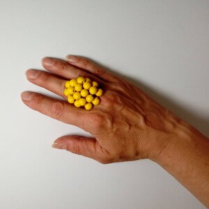 May include: A large yellow ring made of many small round beads. The ring is worn on a person's finger.
