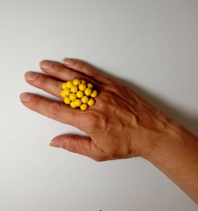 May include: A large yellow ring made of many small round beads. The ring is worn on a person's finger.