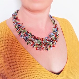 May include: A colorful multi-strand necklace made of small, iridescent glass beads. The beads are arranged in a random pattern, creating a unique and eye-catching design.