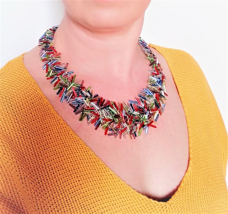 May include: A colorful multi-strand necklace made of small, iridescent glass beads. The beads are arranged in a random pattern, creating a unique and eye-catching design.