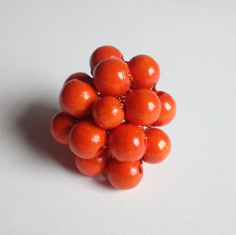 May include: A cluster of orange wooden beads are wired together to form a sphere. The beads are all the same size and are arranged in a random pattern.