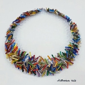 May include: A colorful necklace made of small, glass rods in various colors, including red, blue, green, yellow, and silver. The necklace is arranged in a circle, creating a unique and eye-catching design.