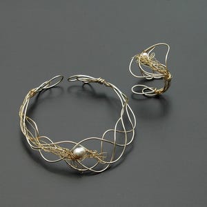 May include: A gold wire necklace and ring set with a single pearl accent. The necklace is a delicate, intricate design with a woven wire pattern. The ring is a simple band with a similar woven wire design.