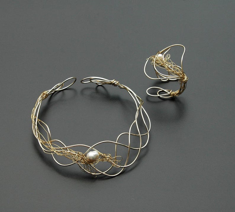 May include: A gold wire necklace and ring set with a single pearl accent. The necklace is a delicate, intricate design with a woven wire pattern. The ring is a simple band with a similar woven wire design.