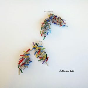 May include: A pair of dangle earrings featuring a cluster of colourful glass beads. The beads are in shades of red, orange, yellow, green, blue, and purple. The earrings are made with silver wire.