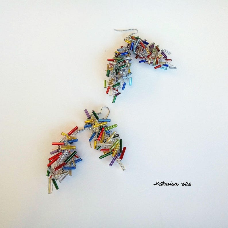 May include: A pair of dangle earrings featuring a cluster of colourful glass beads. The beads are in shades of red, orange, yellow, green, blue, and purple. The earrings are made with silver wire.