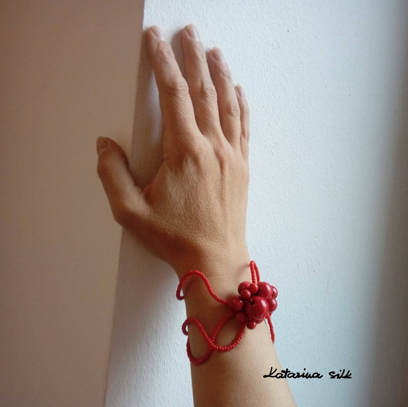 May include: A red beaded bracelet with a large red flower-shaped cluster of beads. The bracelet is on a person's wrist.